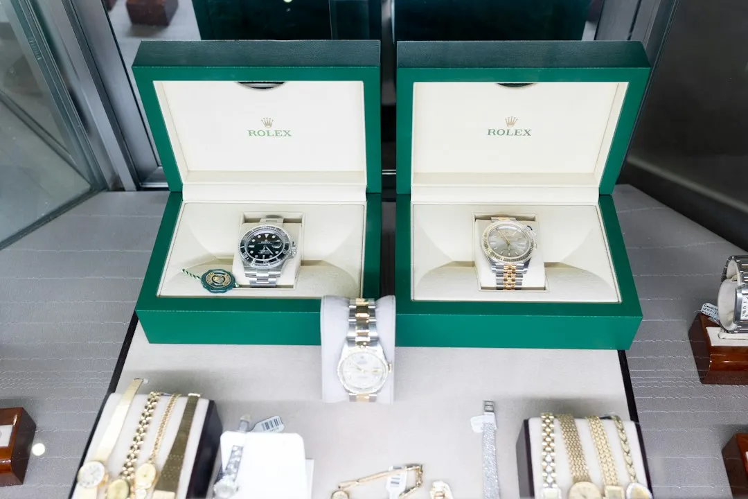 Two open green Rolex boxes displaying luxury wristwatches on a retail counter.