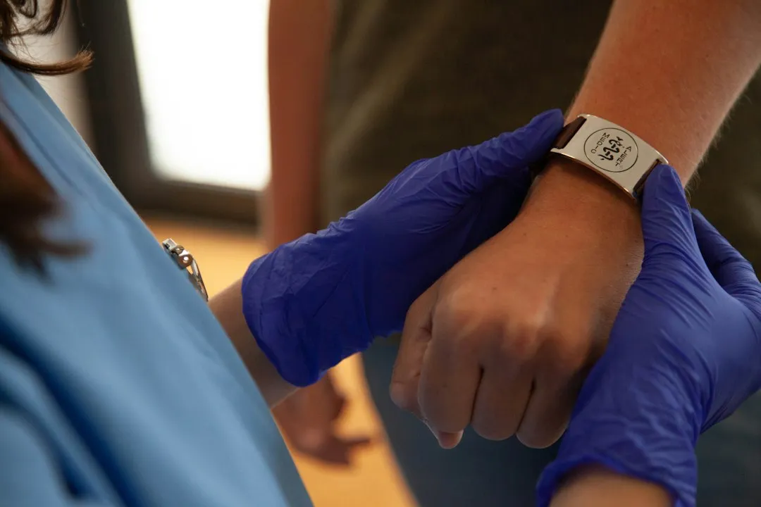 A wrist wearing a watch while being held by hands in blue medical gloves.