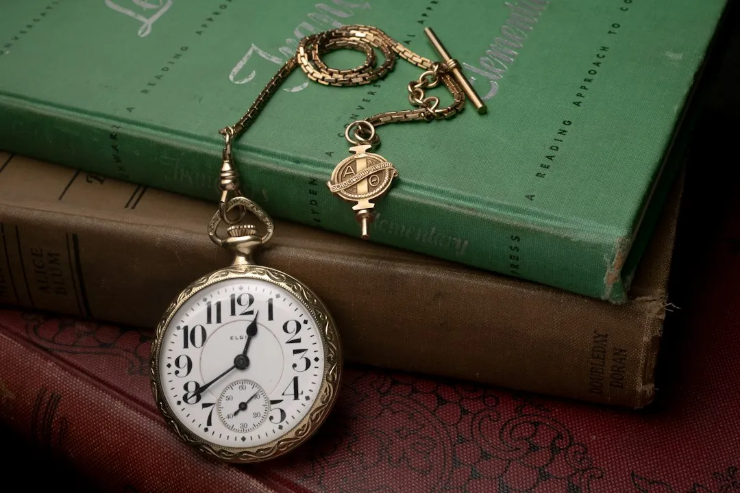 A vintage pocket watch with a gold chain and fob resting on old books.