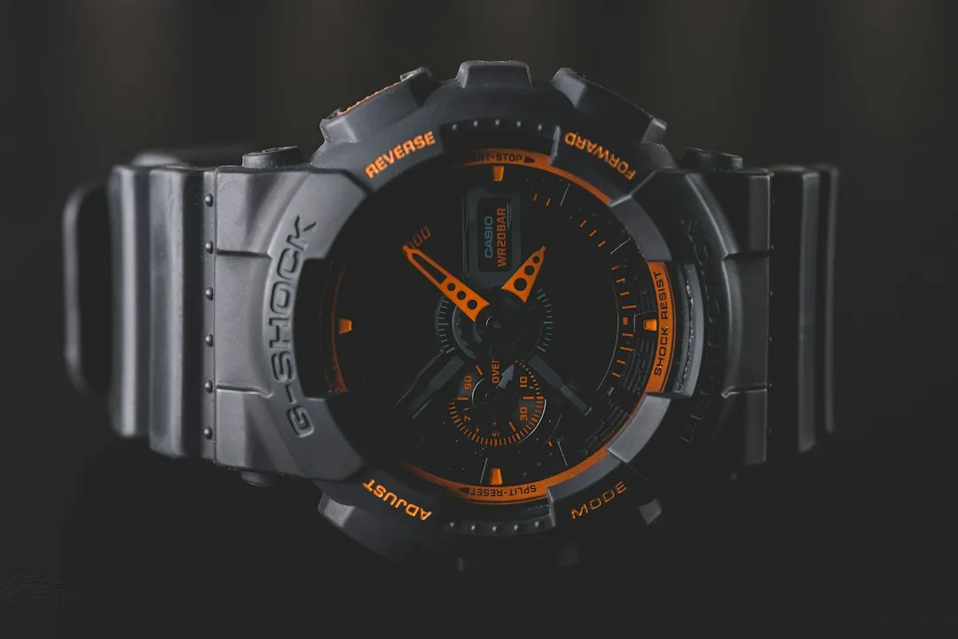 A close-up shot of a black and orange G-Shock wristwatch face against a dark background.