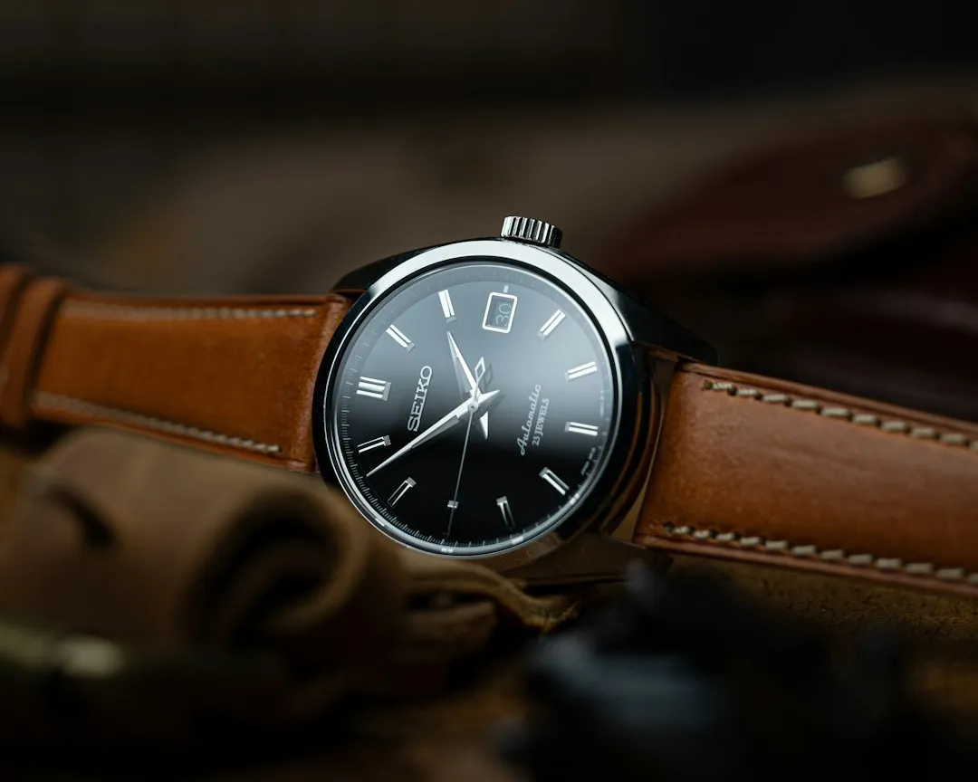 A close-up of a Seiko wristwatch featuring a dark dial and a brown leather strap on fabric.