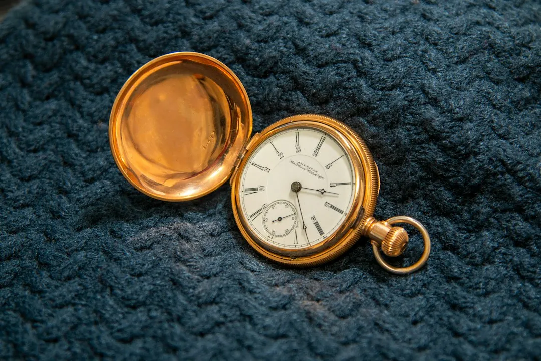 A vintage gold pocket watch with its back cover open resting on blue textured fabric.