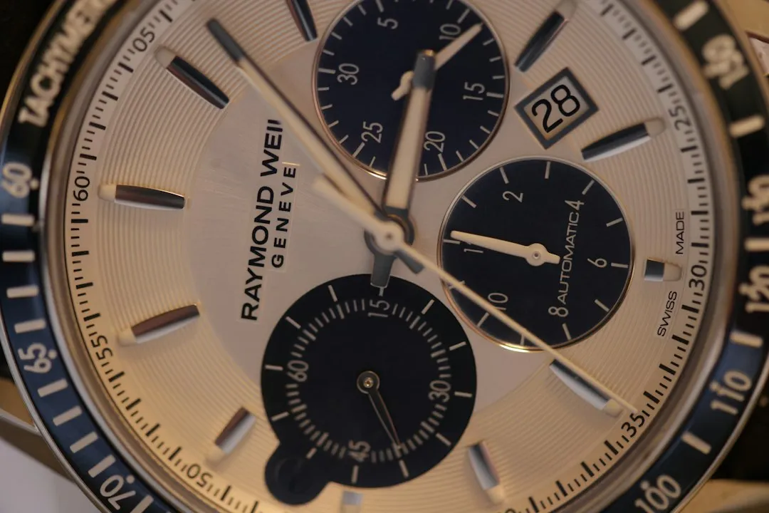A close-up of a Raymond Weil chronograph watch dial featuring a tachymeter scale on the bezel.