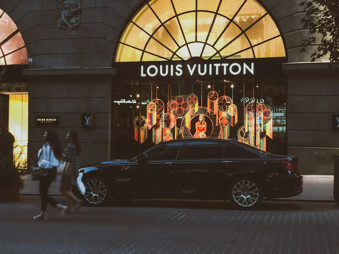 A Louis Vuitton storefront at night featuring a window display with hanging circular timepiece decorations.