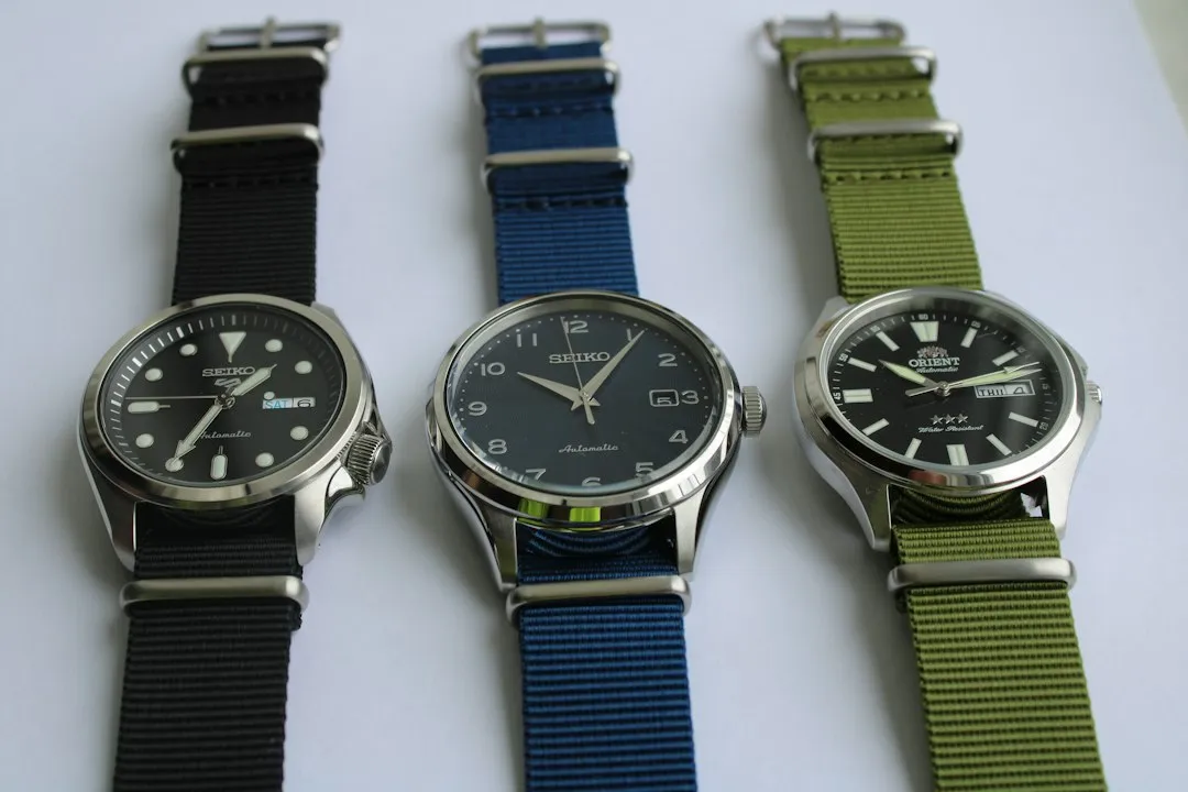 Three wristwatches with black, blue, and green NATO straps displayed on a white background.