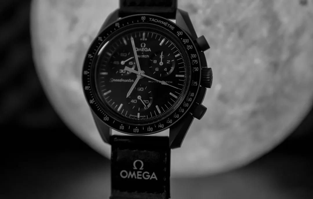 An Omega Speedmaster watch with a black strap displayed against a blurred moon background.
