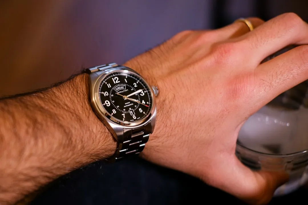 A wrist wearing a silver metal bracelet watch with a black dial and large white Arabic numerals.