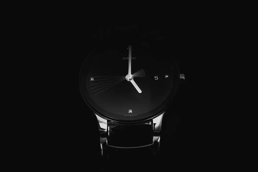 A close-up of a black Rado wristwatch with a minimalist dial against a dark background.
