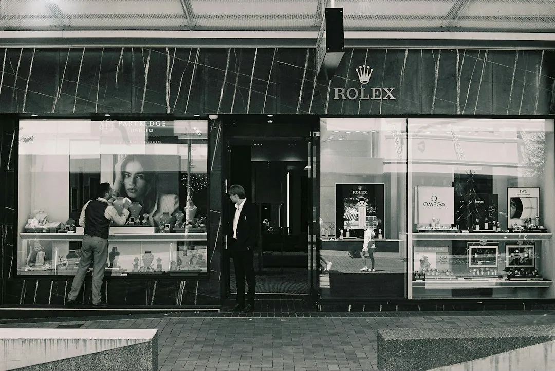 Black and white photo of a Rolex store exterior with watches visible in the display windows.