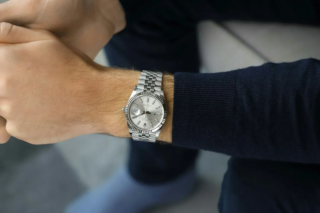 A close-up of a man's wrist wearing a silver Rolex Datejust watch with a fluted bezel.