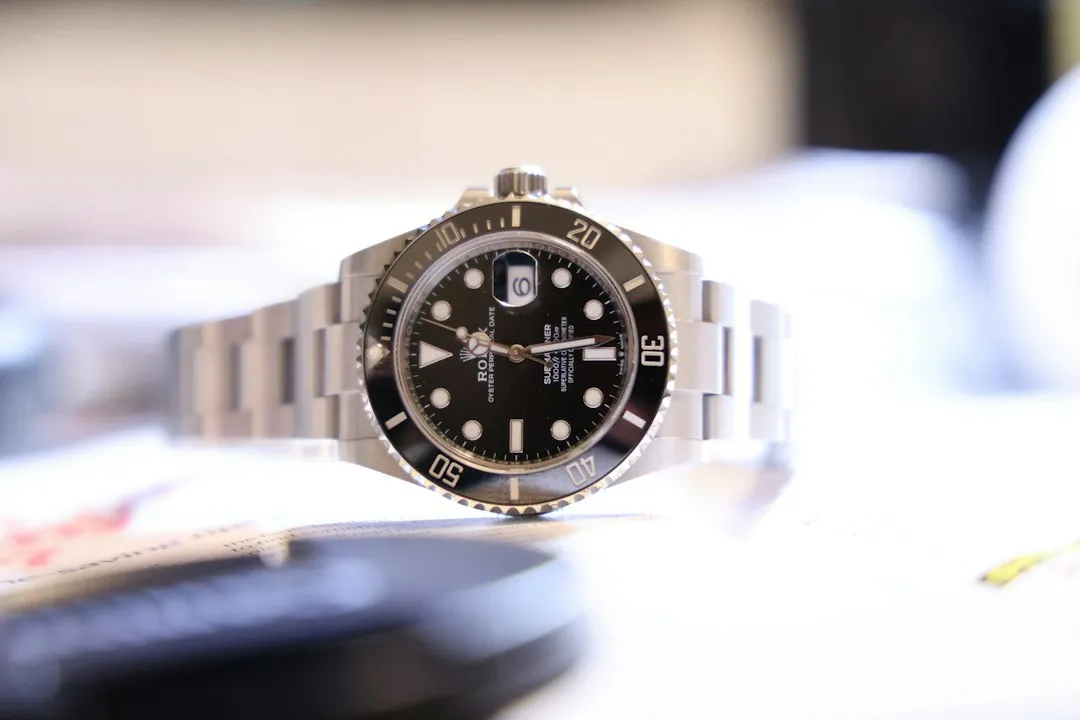 A stainless steel dive watch with a black dial and rotating bezel rests on a white surface.
