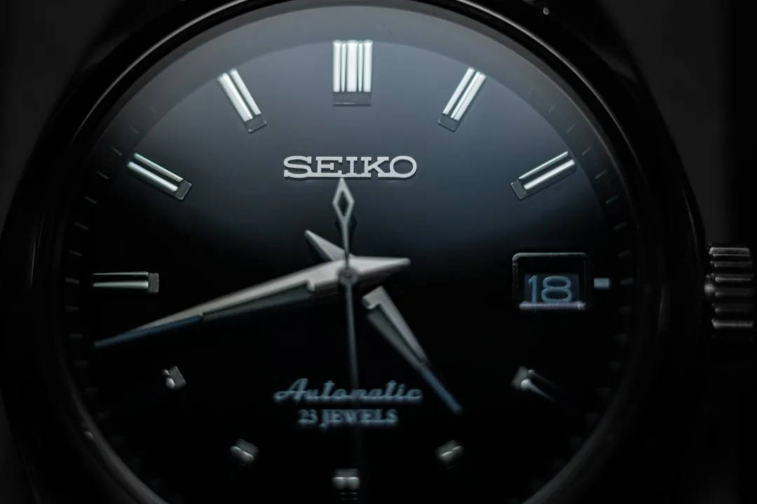 Close-up of a black Seiko automatic watch dial with baton markers and date window.