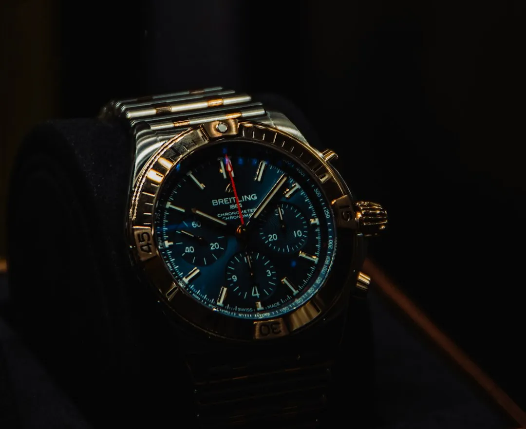 A close-up shot of a blue dial Breitling chronograph wristwatch with a steel bracelet resting on a dark cushion.