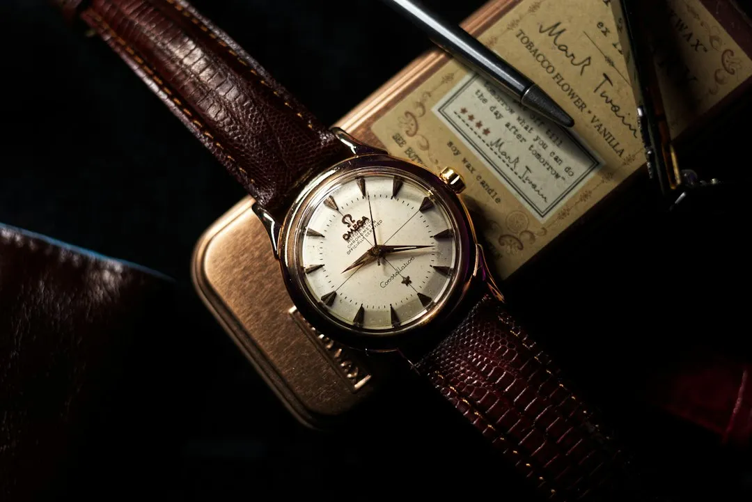 A close-up of a vintage wristwatch with a brown leather strap resting on its original box and papers.