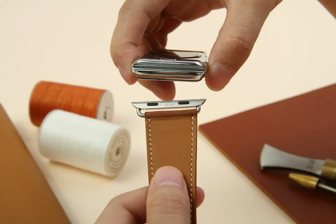 Close-up of hands holding an Apple Watch case above a leather watch strap on a table.
