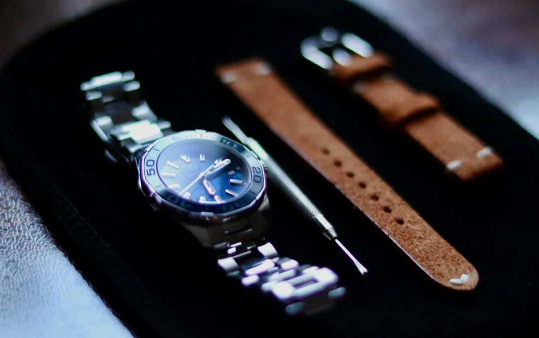 A close-up of a wristwatch with a metal band next to a tool and leather straps.