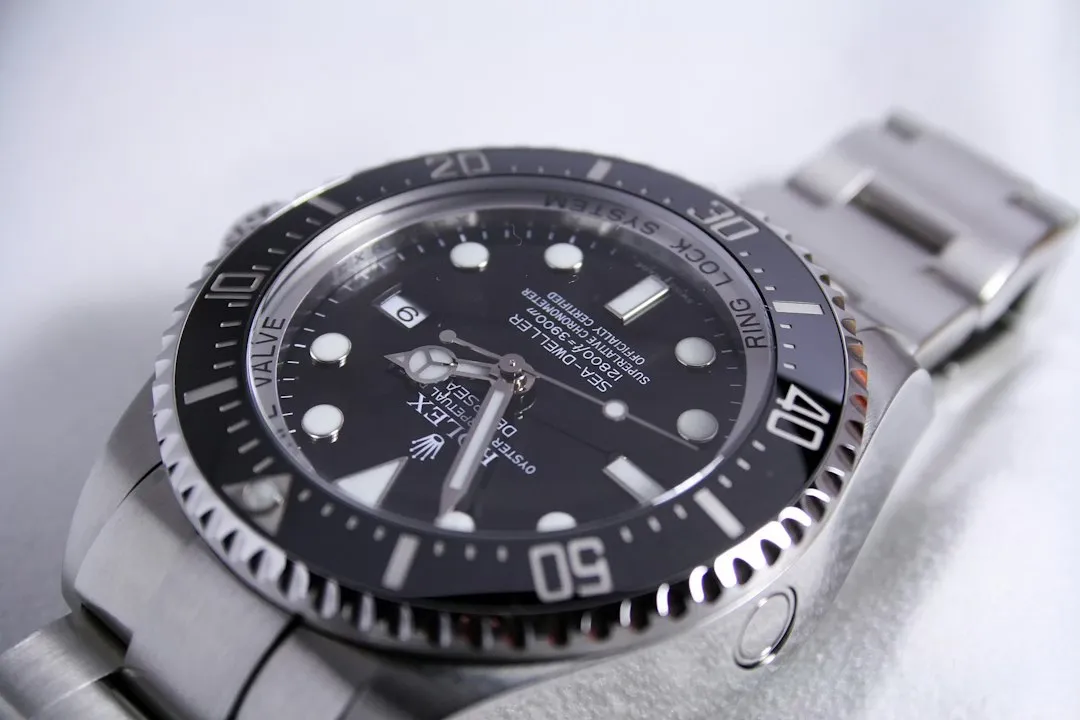 A close-up of a silver wristwatch with a black dial showing the crown on the right side.