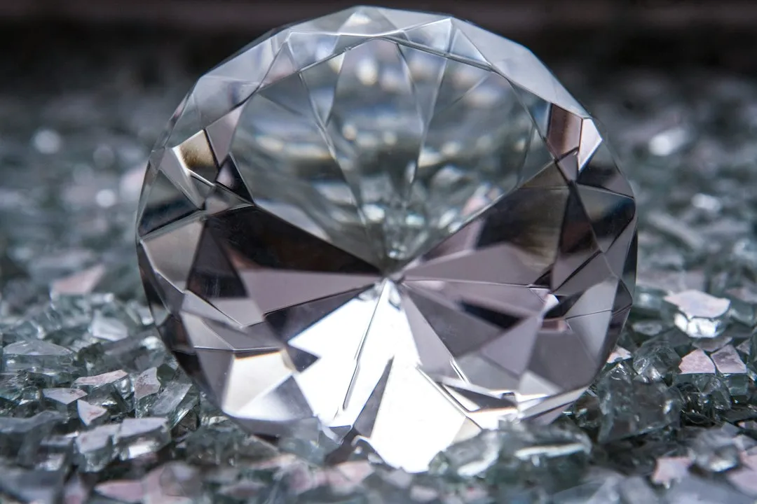 A close-up of a round, faceted sapphire watch crystal resting on abrasive grit.