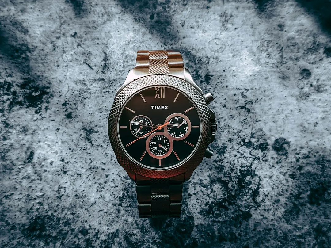 A brown Timex chronograph watch with a metal bracelet resting on a textured grey surface.