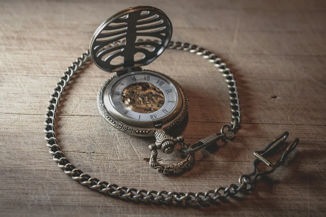 An antique open pocket watch resting on its silver chain with a decorative fob attached on a wooden surface.
