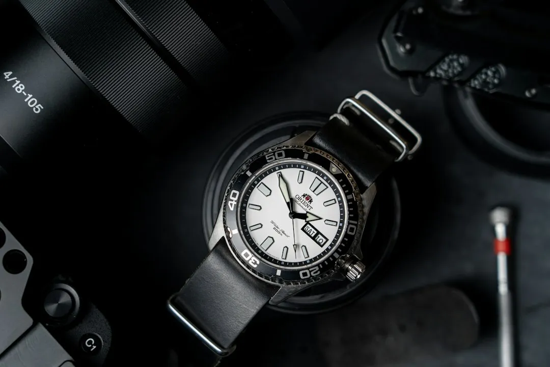 Close-up of a wristwatch with a black strap resting on a table with photography gear.