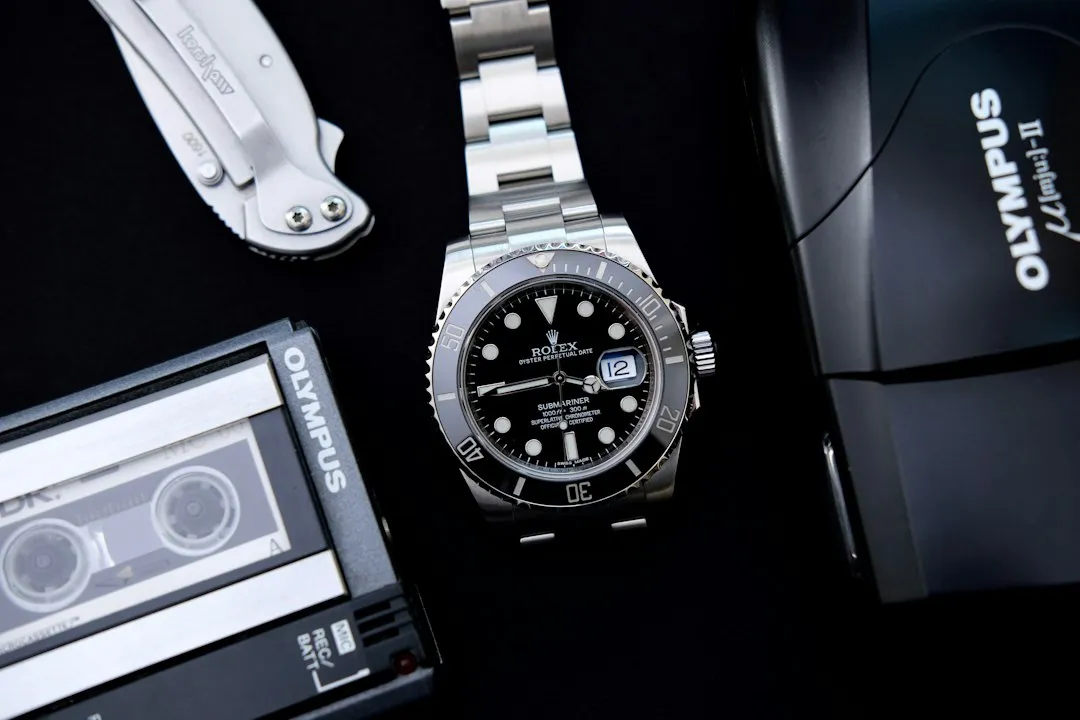 A silver wristwatch with a black dial and metal bracelet rests on a dark surface.