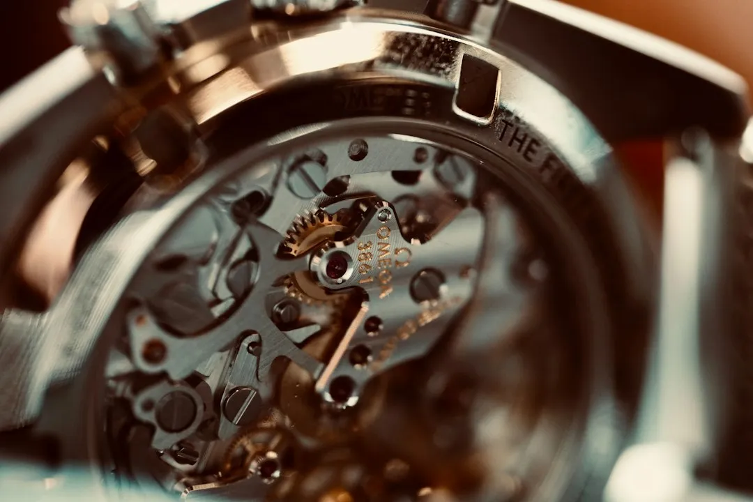 Primer plano de un movimiento de reloj con engranajes y una corona estriada visible en la parte superior izquierda.