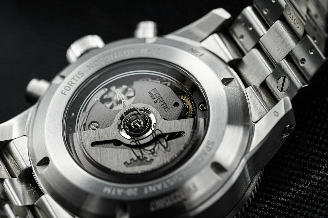 A close-up of a silver wristwatch case back revealing the mechanical movement and engraved text including GMT 24H.