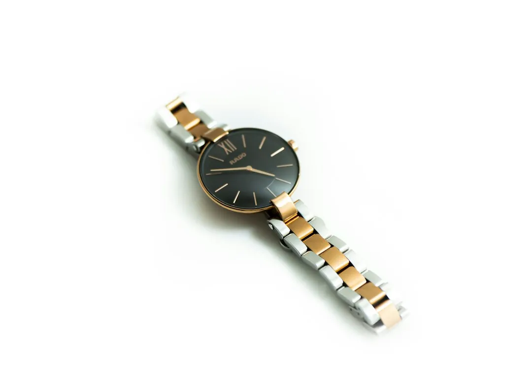 A two-tone wristwatch with a dark dial and metal bracelet on a white background.