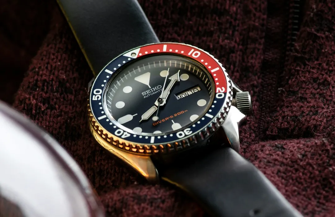 A Seiko automatic diver watch with a black dial and unidirectional bezel resting on a maroon towel.