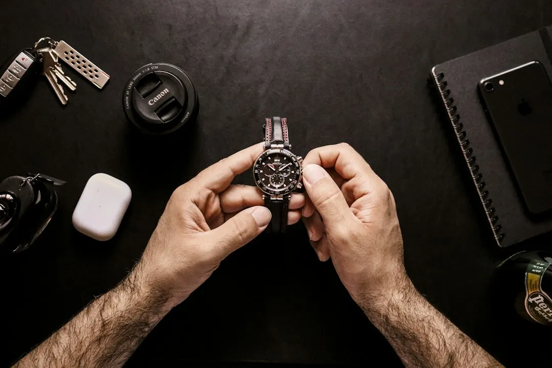 A pair of hands holds a silver wristwatch with a metal link bracelet above a desk.