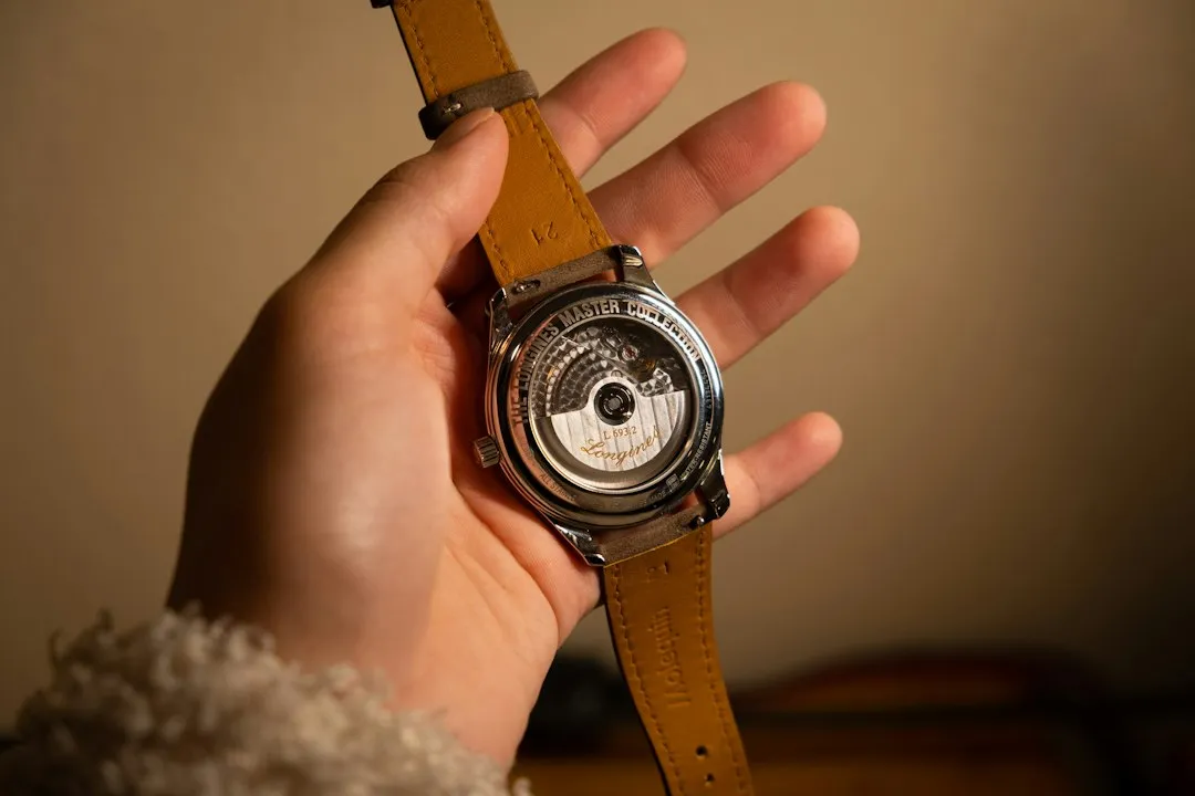 A hand holds a wristwatch with an exhibition case back revealing the automatic movement rotor.