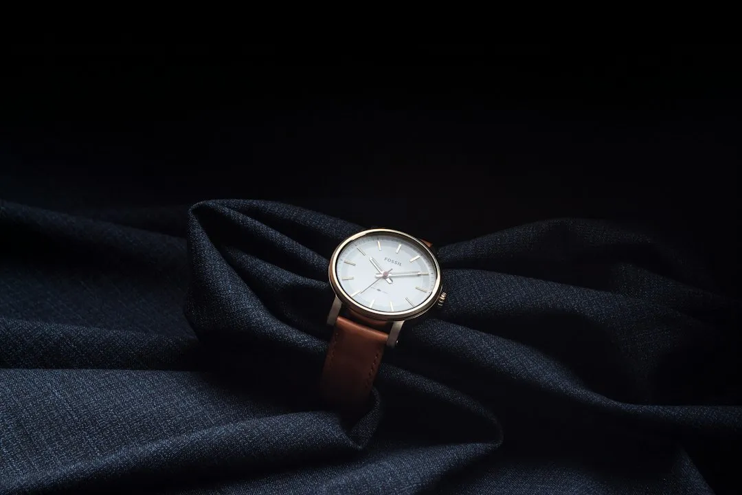 A gold-cased wristwatch with a brown leather strap resting on dark blue suit fabric.