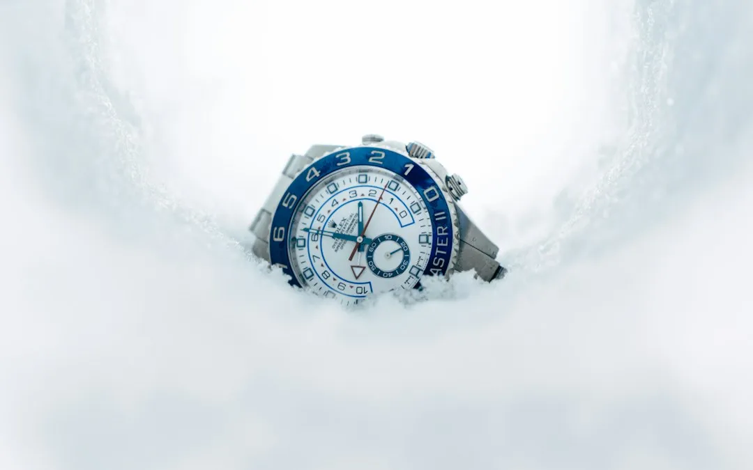 A wristwatch partially buried in white snow, showing its blue and white dial clearly.