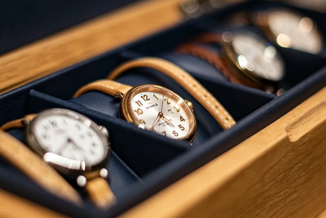 A close-up of a wooden watch box with watches resting on blue cushioned slots.